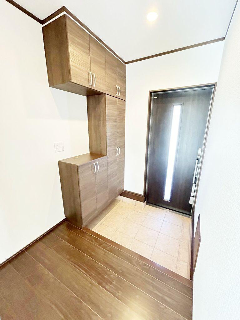 玄関スペースはタイル床と木目調の収納があり、採光窓付きのドアで明るい印象です。