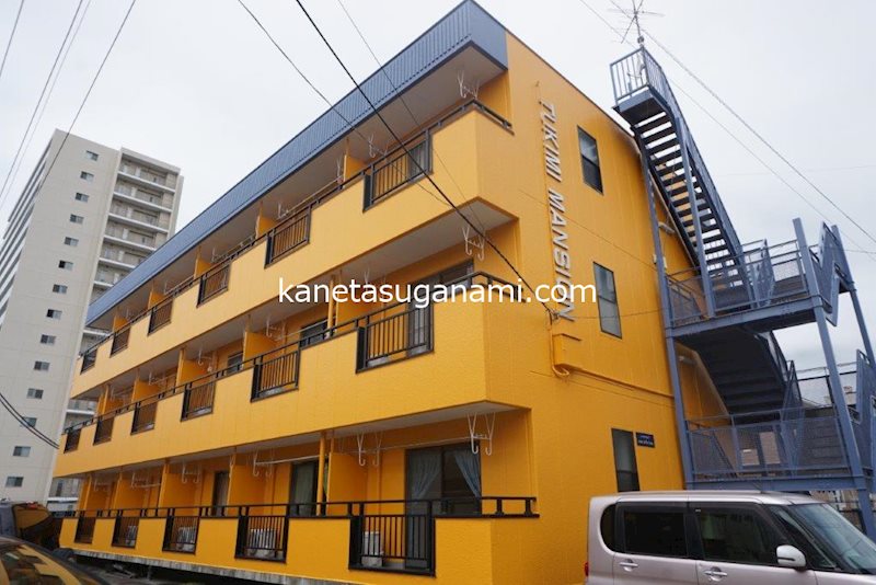 建物外観　オレンジ色の建物に落ち着いた青色の差し色階段が印象的な物件で